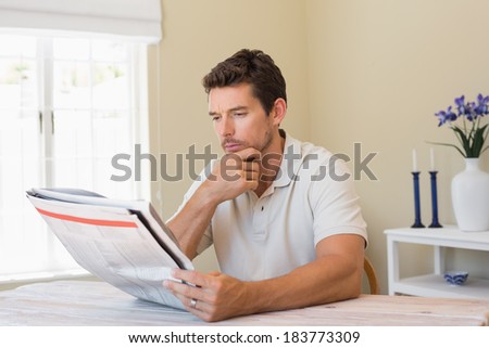 Concentrated young man reading newspaper at home