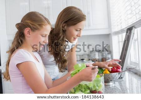 Side view of a girl helping mother to cut vegetables in the kitchen at home