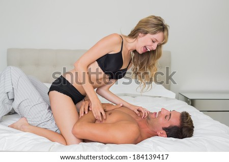 Side view of a cheerful romantic young couple in underwear in bed at home
