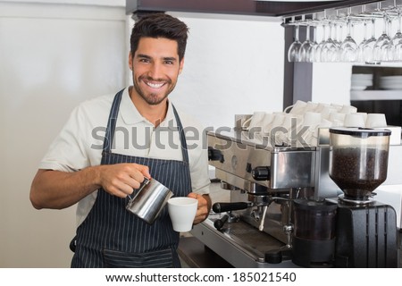 Portrait of a young waiter smiling and making cup of coffee at coffee shop