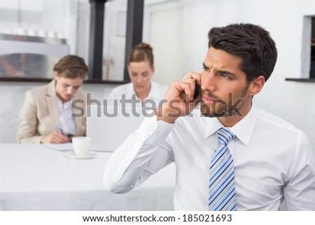 Businessman using mobile phone with colleagues in meeting behind at office desk