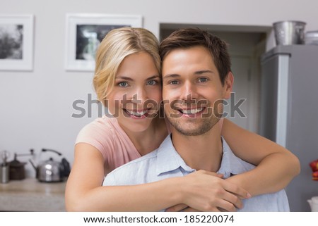 Portrait of a smiling young woman embracing man from behind in kitchen at home
