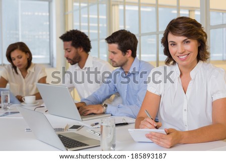 Portrait of a smiling young businesswoman writing notes with colleagues in meeting at the office