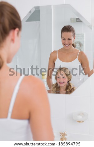 Portrait of a happy mother and daughter looking at bathroom mirror in the house