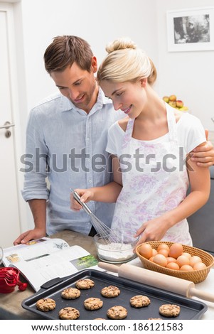 Young couple looking at cook book and preparing cookies in the kitchen at home