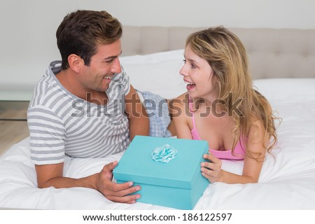 Young man giving surprised woman gift box in bed at home