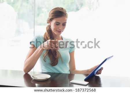 Smiling young woman with coffee cup using digital tablet at counter in the coffee shop