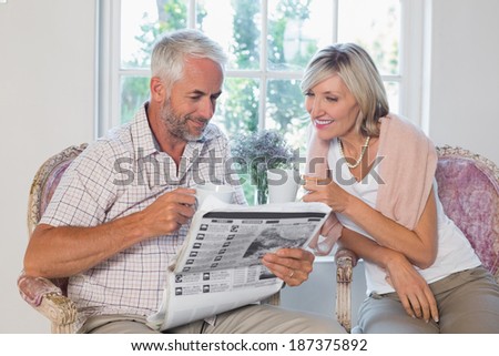 Mature couple reading newspaper while drinking coffee at home
