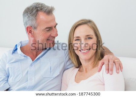 Happy relaxed couple sitting on sofa with arm around at home