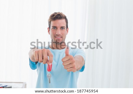 Portrait of a young man holding out new house key while gesturing thumbs up