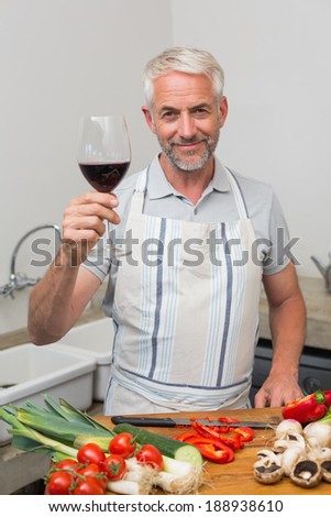 Portrait of a mature man with wine glass while chopping vegetables in the kitchen at home