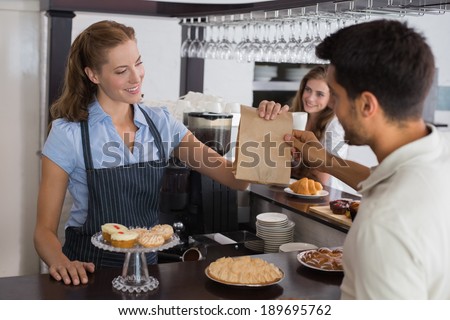 Friendly female cafe owner giving packed food to a couple at the coffee shop