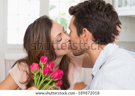 Side view of a loving young couple kissing with flowers in hand at home