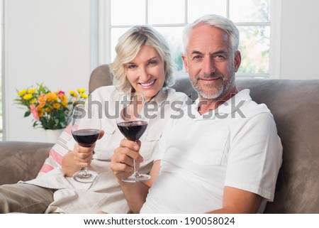 Portrait of a happy mature couple with wine glasses in the living room at home