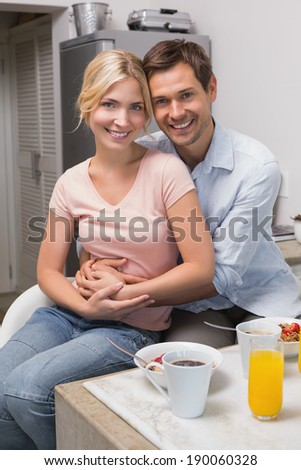 Portrait of a happy young man embracing woman from behind at breakfast table at home