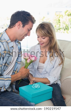 Loving young couple with flowers and gift box sitting on sofa at home