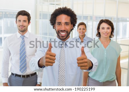 Portrait of a young businessman with colleagues gesturing thumbs up in the office