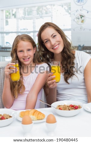 Portrait of happy mother and daughter having breakfast in the kitchen at home