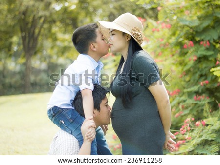 Asians father and son kissing her pregnant wife tummy.