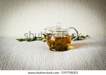 Green tea in glass teapot with fresh dry mint leaves on textured linen background. Image with dark vignette effect