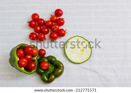 Small tomatoes in cut green pepper with zucchini slice at white linen background. Horizontal image