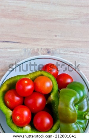 Small tomatoes in cut green pepper on white dish at wooden background. Vertical image