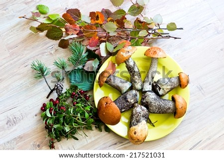 Fresh mushrooms with leaves and cranberry in yellow dish on wooden background