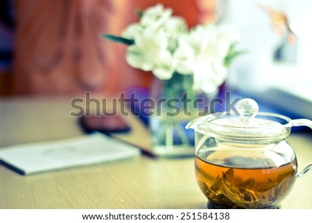 Celebrating composition: bouquet of white freesia flowers, smartphone, pen, teapot and notebook with painted heart. Selective focus on teapot. Horizontal vintage image, multicolored bokeh background