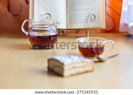Still life composition: morning tea in glass cup and teapot with sweet cake and reading book.Selective focus on teapot and blurred background