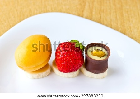 Fresh fruits and berries mix: strawberry, apricot, banana and candy on white dish