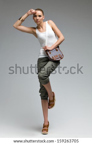 Beautiful fashion model posing in high heels with bag. Studio shot on gray background.