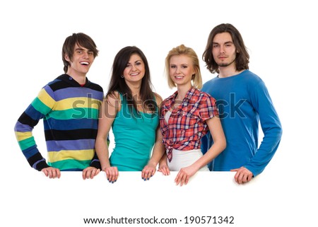 Four young students standing behind white blank banner and smiling. Waist up studio shot isolated on white.