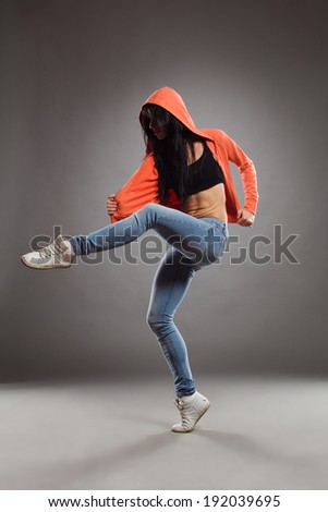 The dancer in a hood. Female dancer posing standing on one leg. Full length studio shot on gray background.