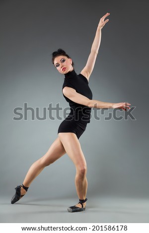 Female ballet dancer is posing in legs apart and arms raised. Full length studio shot on gray background.