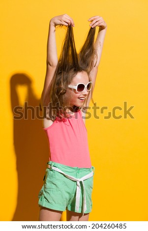 Smiling girl fool around. Smiling little girl pulling her hair. Three quarter length studio shot on yellow background.