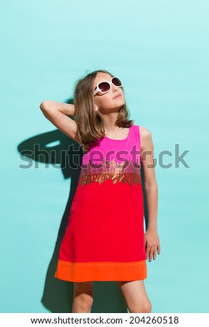 Little miss sunshine. Young fashionable girl in sunglasses posing in sunlight. Three quarter length studio shot on teal background.