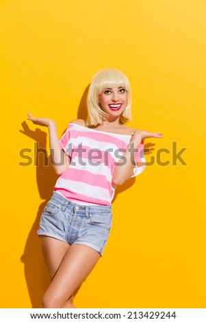 Smiling blonde spread her hands and looking up. Three quarter length studio shot on yellow background.