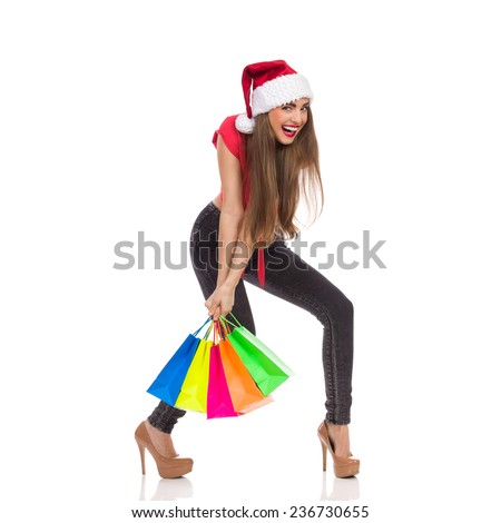 Christmas sale. Smiling christmas girl carrying heavy colorful shopping bags. Full length studio shot isolated on white.