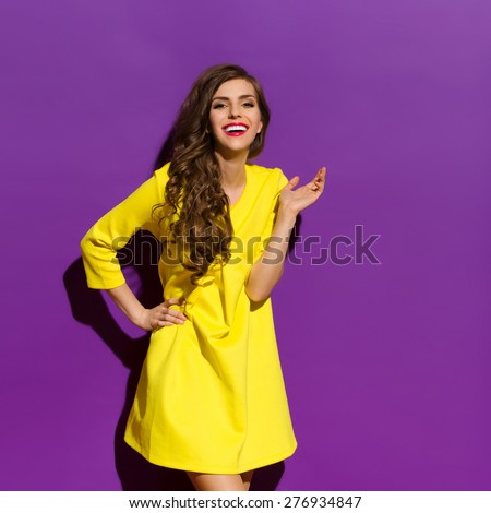 Beautiful happy girl posing in yellow mini dress. Three quarter length studio shot on violet background.