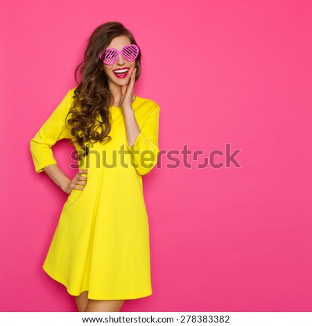 Curious Girl In Pink Sunglasses. Smiling beautiful girl in pink sunglasses and yellow mini dress holding hand on chin and looking away. Three quarter length studio shot on pink background.