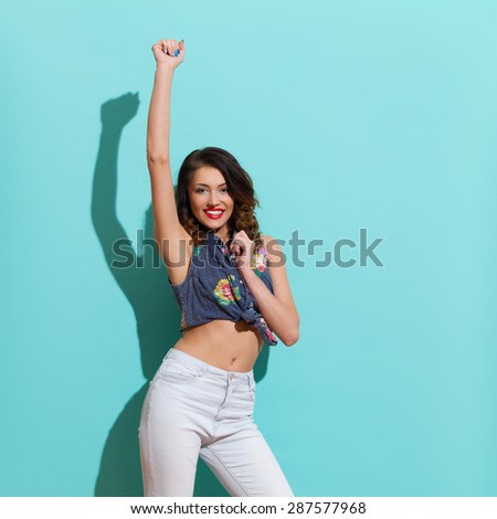 I Did It. Happy young woman posing with arm raised. Three quarter length studio shot on teal background.