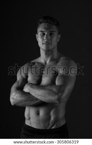 Muscular Man Portrait. Closeup of muscular man with arms crossed. Black and white studio shot on black background.