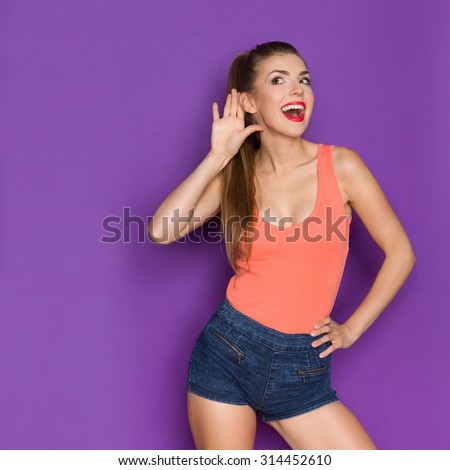 Can You Speak Louder. Young woman in orange shirt eavesdrops. Three quarter length studio shot on turquoise background.