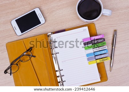 surface of a wooden table with notebook, smartphone, eye glasses, and pen, top view