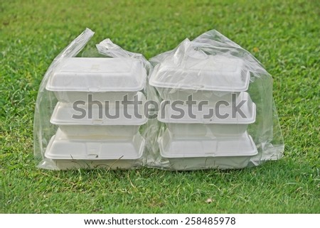 a clear plastic bags containing three foam containers on green grass background