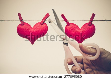 Scissors cutting a rope with two red hearts - Broken heart concept