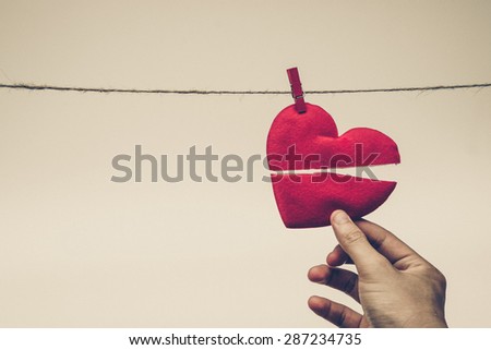 hand holding broken red heart hung on rope
