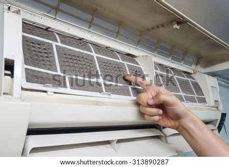 hand pointing at a very dirty air-conditioner filter that needs cleaning