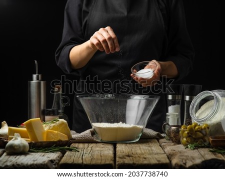 The chef prepares dough for pasta, focaccia, bread, pizza. He adds salt to the dough. There are many ingredients on the wooden table. Restaurant, hotel, recipe book. Foto stock © 