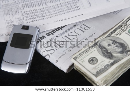 business section of the newspaper, a cellular phone and a stack of one hundred dollar bills laying on the table